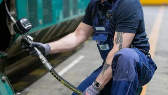 Mechatroniker führt Wartungsarbeiten an einem ODEG-Zug im Werkstattbereich durch und überprüft technische Komponenten mit einem Schlauchsystem