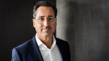 Alexander Sterr, Geschäftsführer der NETINERA Deutschland GmbH, in einem Business-Porträt mit elegantem dunkelblauem Anzug und weißem Hemd vor modernem, grauem Hintergrund.