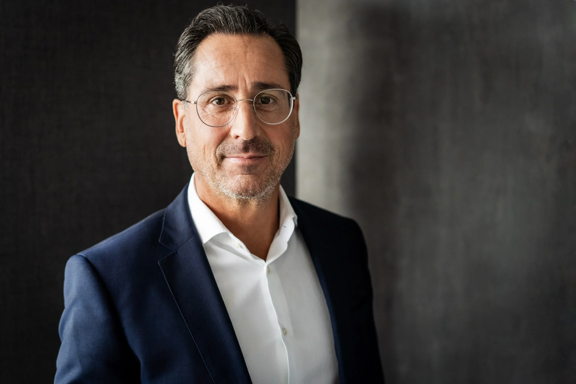 Alexander Sterr, Geschäftsführer der NETINERA Deutschland GmbH, in einem Business-Porträt mit elegantem dunkelblauem Anzug und weißem Hemd vor modernem, grauem Hintergrund.