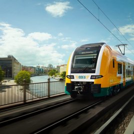 Moderner Regionalzug der ODEG fährt über eine Brücke in Berlin mit Blick auf die Spree und Stadtgebäude