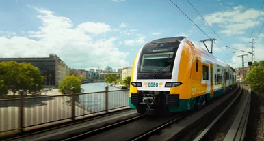 Moderner Regionalzug der ODEG fährt über eine Brücke in Berlin mit Blick auf die Spree und Stadtgebäude