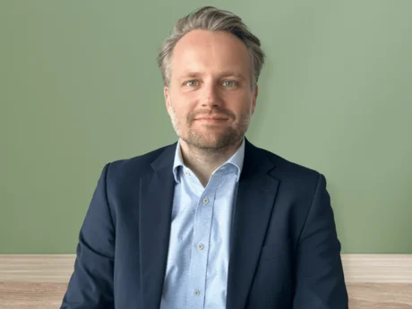 Robert von der Heide, Referent Unternehmenskommunikation bei NETINERA Deutschland GmbH, in einem professionellen Business-Porträt vor grünem Hintergrund, mit dunkelblauem Sakko und hellblauem Hemd.