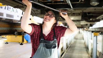 Person führt Wartungsarbeiten unter einem Zug in einer Werkstatt durch und nutzt einen Schraubenschlüssel für die Instandhaltung