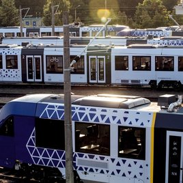 Mehrere moderne vlexx-Züge stehen auf Gleisen in einem Rangierbahnhof bei Tageslicht, umgeben von Oberleitungen und Technik