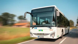 Moderner weißer Linienbus der Marke Iveco fährt auf einer Landstraße durch grüne Landschaft, mit Logos von KVG und hvv auf der Front.