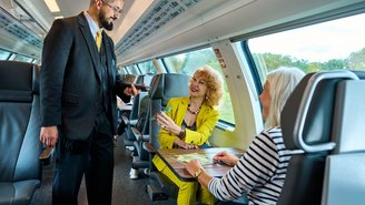 Zugbegleiter kontrolliert Fahrkarten von zwei Reisenden im komfortablen Innenraum eines modernen Doppelstockzugs