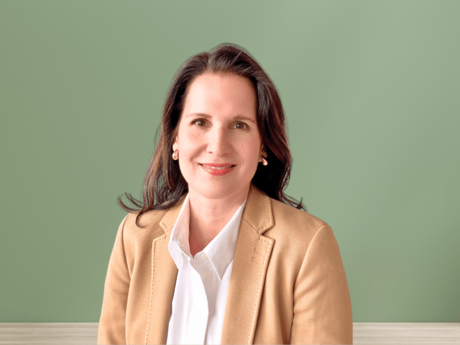 Nina Massek, Referentin Unternehmenskommunikation bei NETINERA Deutschland GmbH, in einem professionellen Porträt vor grünem Hintergrund, mit beigem Blazer und weißer Bluse.