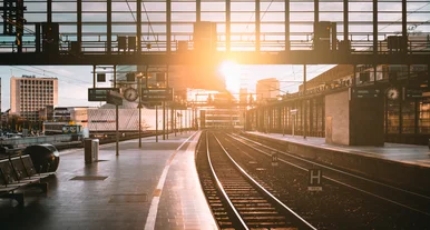 „Leerer Bahnhof Zoologischer Garten mit Gleisen und moderner Glasfassade bei Sonnenaufgang, Lichtstrahlen spiegeln sich auf dem Bahnsteig.