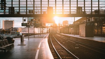 „Leerer Bahnhof Zoologischer Garten mit Gleisen und moderner Glasfassade bei Sonnenaufgang, Lichtstrahlen spiegeln sich auf dem Bahnsteig.