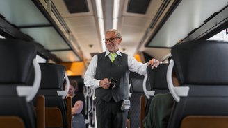 Zugbegleiter steht im Mittelgang eines modernen Regionalzugs und führt Fahrkartenkontrolle durch