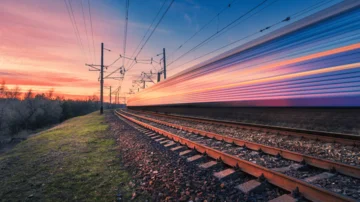 Schnell fahrender Zug auf elektrifizierter Bahnstrecke bei Sonnenuntergang, mit dynamischer Bewegung und farbenfrohem Himmel, symbolisch für moderne Mobilität und Hochgeschwindigkeitsverkehr.