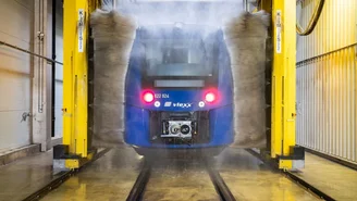 Blauer vlexx-Zug wird in einer automatischen Waschanlage gereinigt, Wasserstrahlen und Bürsten entfernen Schmutz von der Zugoberfläche