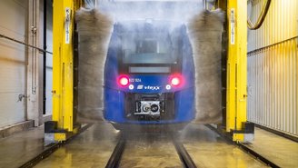 Blauer vlexx-Zug wird in einer automatischen Waschanlage gereinigt, Wasserstrahlen und Bürsten entfernen Schmutz von der Zugoberfläche