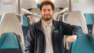 Person in erixx-Jacke steht vor einem blau-türkisen Regionalzug mit der Aufschrift ‚Schleswig-Holstein. Der echte Norden.‘ am Bahnsteig.