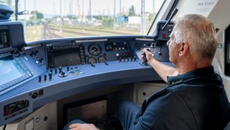 Lokführer sitzt im Führerstand eines modernen Zuges und bedient die Steuerungselemente mit Blick auf die Gleise