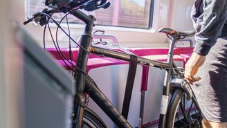 Schwarzes Fahrrad steht sicher befestigt im Innenraum eines modernen Regionalzugs, neben einem großen Fenster mit Blick auf die vorbeiziehende Landschaft.