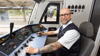 Lokführer sitzt im Führerstand eines modernen Zuges und bedient die Steuerungselemente, mit Blick auf die Instrumententafel und Gleise im Hintergrund.