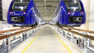 Zwei blaue vlexx-Züge stehen in einer modernen Werkstatthalle auf erhöhten Gleisen für Wartungsarbeiten