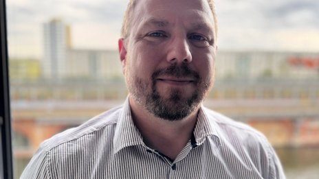 Matthias Bayer, Leiter Operations Management bei NETINERA Deutschland GmbH, in einem Business-Porträt vor einer Fensterfront mit Blick auf Stadt und Fluss.