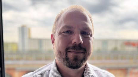 Matthias Bayer, Leiter Operations Management bei NETINERA Deutschland GmbH, in einem Business-Porträt vor einer Fensterfront mit Blick auf Stadt und Fluss.
