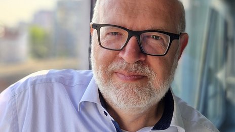 Paolo Bialetti, Leiter Rechnungswesen bei NETINERA Deutschland GmbH, in einem modernen Büro mit Glasfront und Blick auf die Stadt.