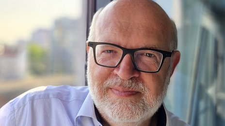 Paolo Bialetti, Leiter Rechnungswesen bei NETINERA Deutschland GmbH, in einem modernen Büro mit Glasfront und Blick auf die Stadt.