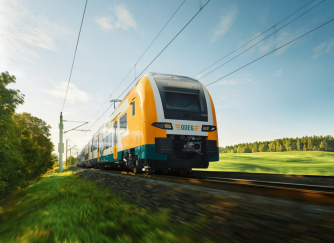 Moderner Elektrozug fährt auf sonniger Strecke durch grüne Landschaft mit Bäumen und Wiesen