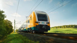 Moderner Elektrozug fährt auf sonniger Strecke durch grüne Landschaft mit Bäumen und Wiesen