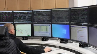Mitarbeiter überwacht Zugverkehr in einer Leitstelle mit mehreren Monitoren, Anzeige von Streckendaten, Fahrplänen und Betriebsinformationen.