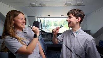 Zwei Personen in Uniform üben Kommunikation mit Mikrofonen im Führerstand eines modernen Zuges