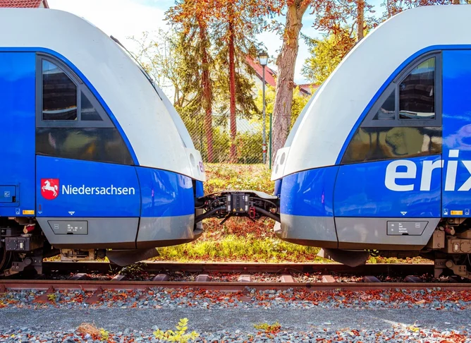 Zwei blau-graue Regionalzüge sind seitlich gekuppelt auf einem Gleis, mit sichtbarer Kupplung und Herbstbäumen im Hintergrund.