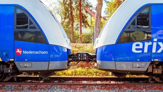 Zwei blau-graue Regionalzüge sind seitlich gekuppelt auf einem Gleis, mit sichtbarer Kupplung und Herbstbäumen im Hintergrund.