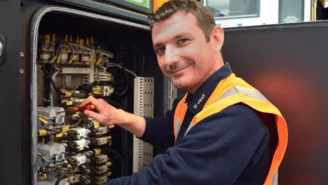 Techniker führt Wartungsarbeiten an elektrischen Komponenten eines Zuges in einem geöffneten Schaltschrank durch