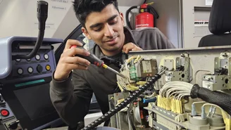 Techniker arbeitet mit einem Schraubendreher an elektronischen Komponenten im Führerstand eines Zuges und überprüft Kabelverbindungen