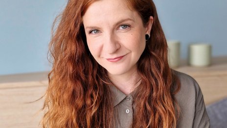 Laura Bönsch, Talent Acquisition Manager bei NETINERA Deutschland GmbH, in einem modernen Bürosetting mit hellblauer Wand und dekorativen Elementen im Hintergrund.